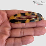 Hand holding a Tokyo hair clip with gold accents on a white background, featuring the brand 'French Amie'.