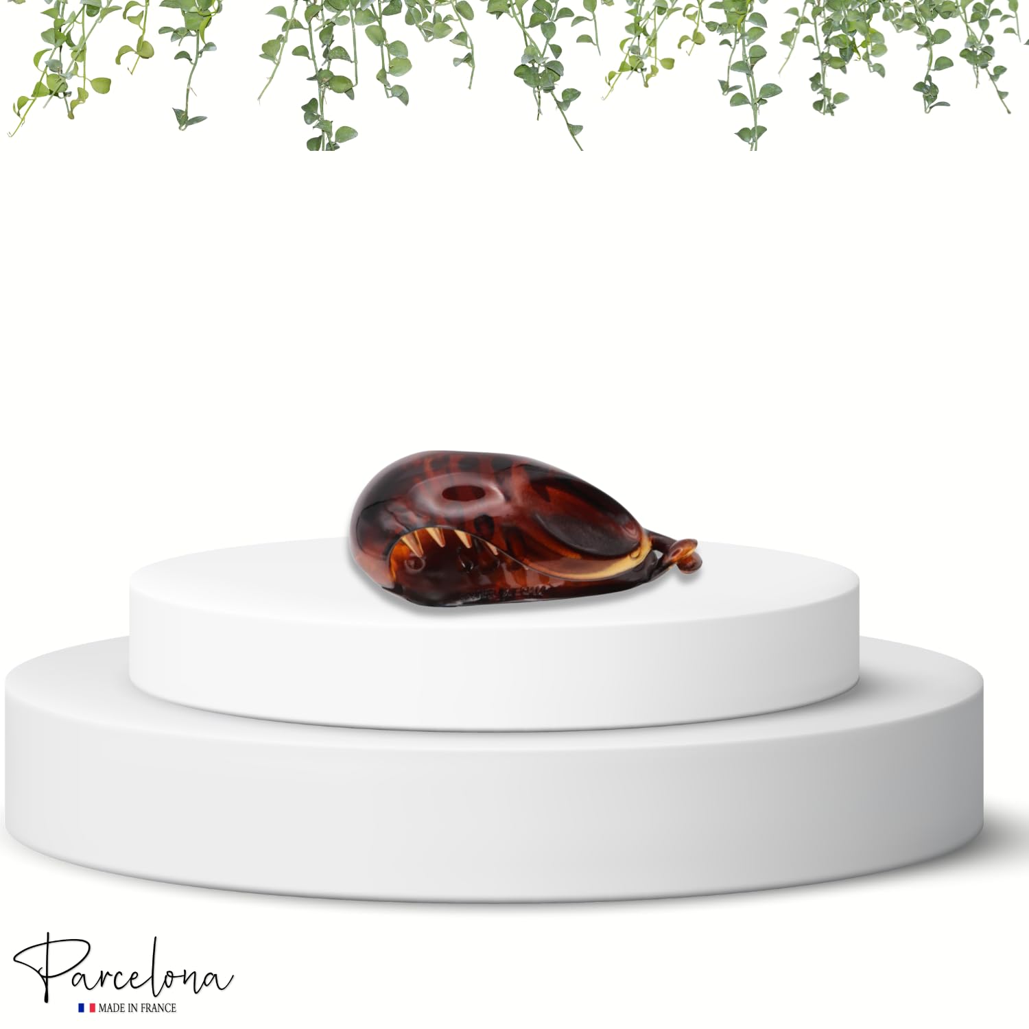 Tortoiseshell clutch on a white pedestal with greenery above, featuring the 'Parcelona' brand.