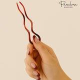 Hand holding a tortoiseshell hair clip against a beige background with 'Parcelona' branding.