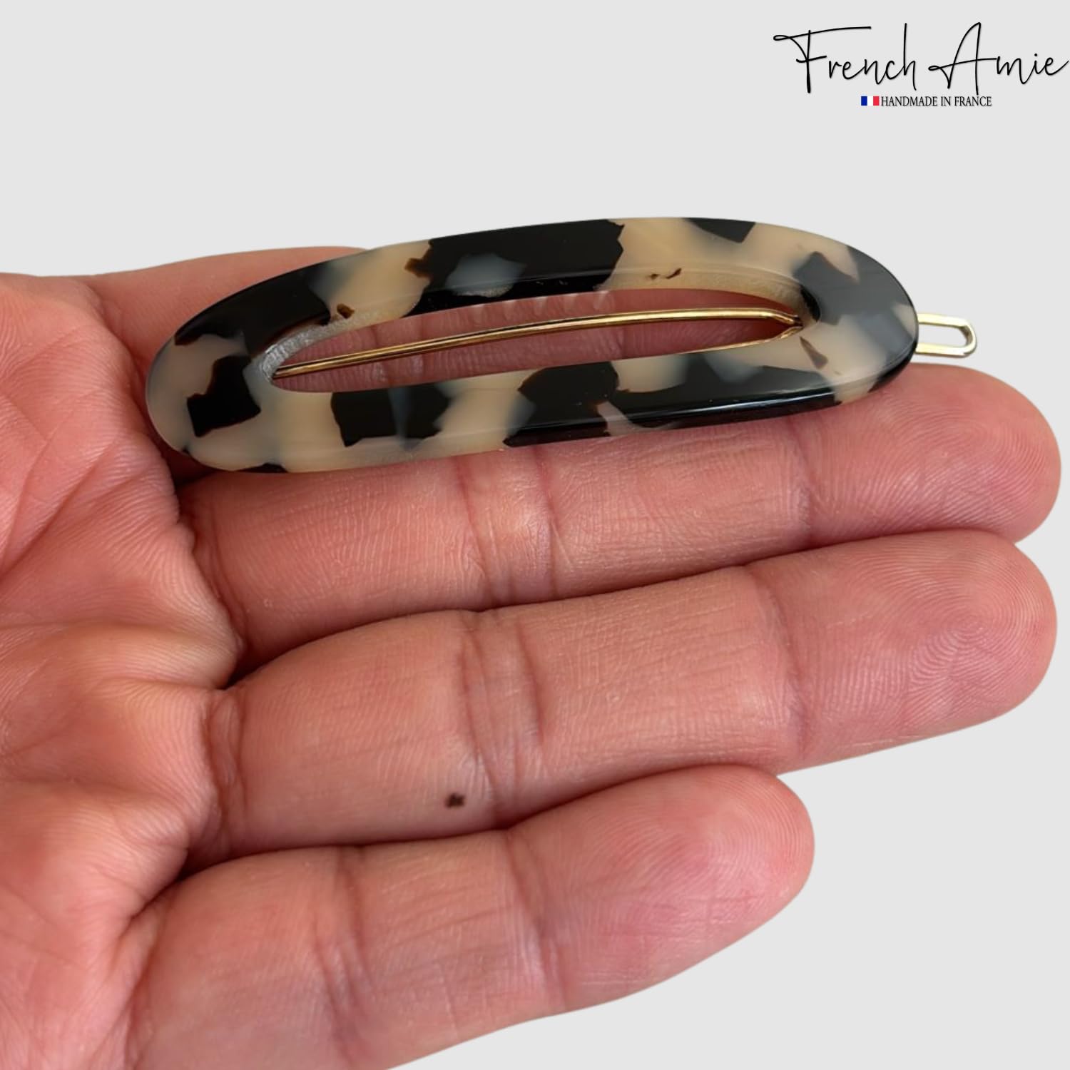 Holding a white Tokyo-patterned hair clip with 'French Amie' branding on a white background
