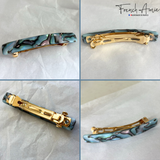 Collage of four views of a hair clip with gold and marble design on a textured white background.