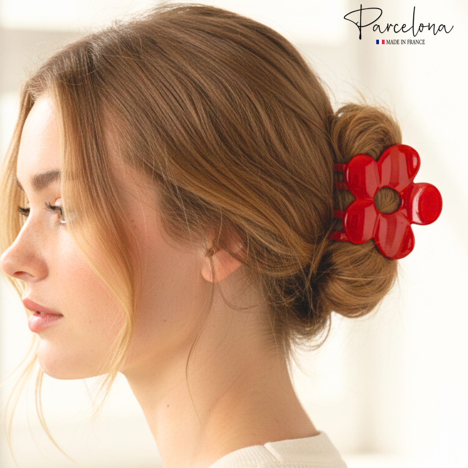Woman with a bun holding a red flower hair accessory, with 'Parcelona' brand logo.